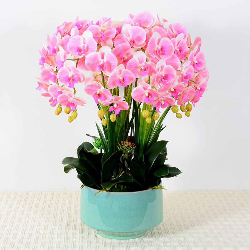 A lush arrangement of artificial pink orchids with yellow buds in a simple white pot, featuring vibrant green leaves and small succulents. What are the best tips for maintaining artificial flowers to keep them looking fresh?