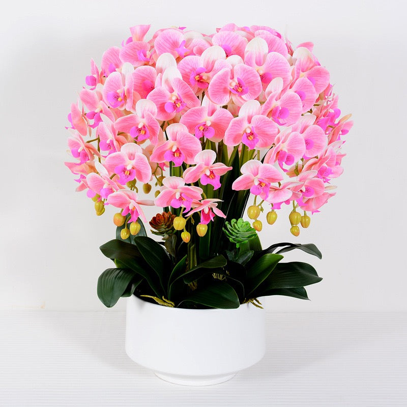 A lush arrangement of artificial pink orchids with yellow buds in a simple white pot, featuring vibrant green leaves and small succulents. What are the best tips for maintaining artificial flowers to keep them looking fresh?