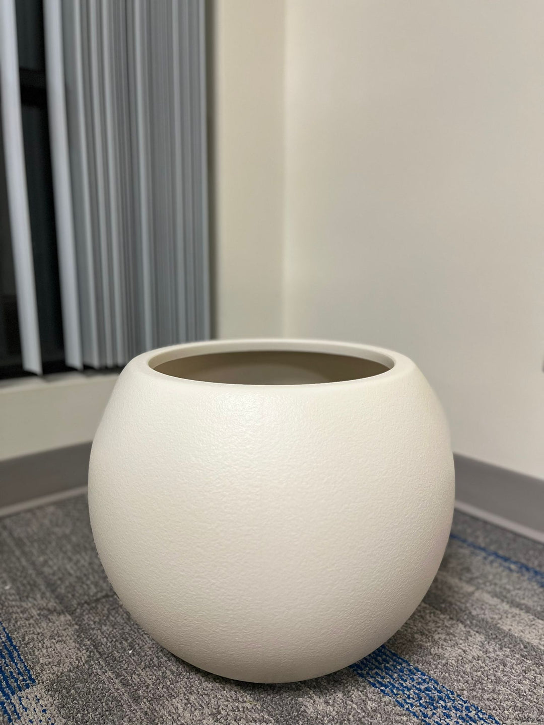 Minimalist ivory round planter with a smooth matte finish, displayed empty indoors on a carpeted floor near a window. What is the planter's capacity in liters?