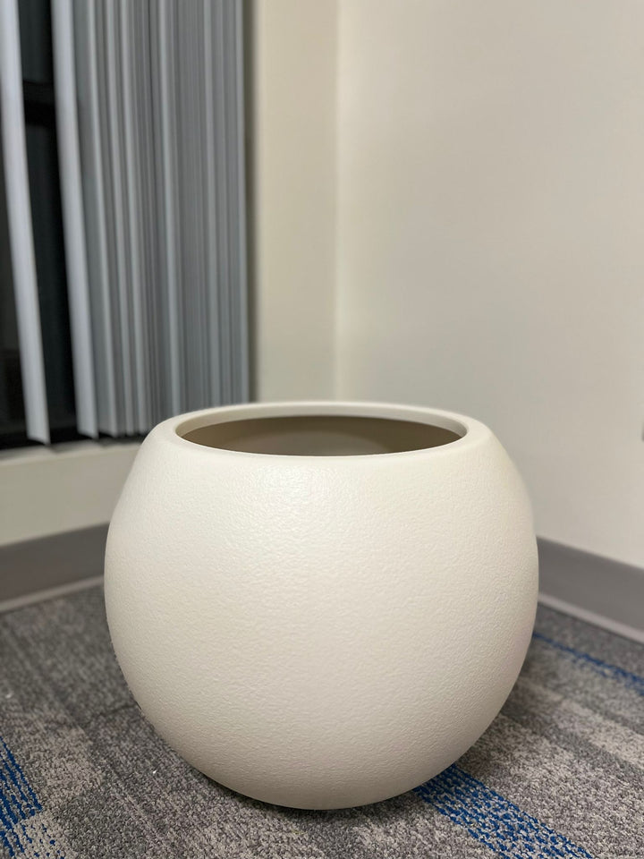 Minimalist ivory round planter with a smooth matte finish, displayed empty indoors on a carpeted floor near a window. What is the planter's capacity in liters?