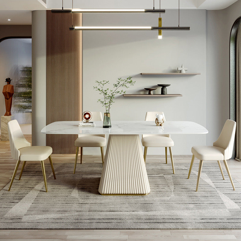Elegant rectangular marble dining table with a fluted pedestal base, complemented by four cream upholstered chairs with gold legs, set in a modern dining room with minimalist decor and contemporary lighting.