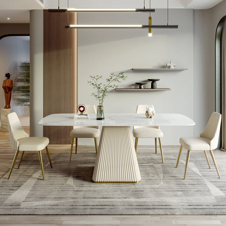Elegant rectangular marble dining table with a fluted pedestal base, complemented by four cream upholstered chairs with gold legs, set in a modern dining room with minimalist decor and contemporary lighting.