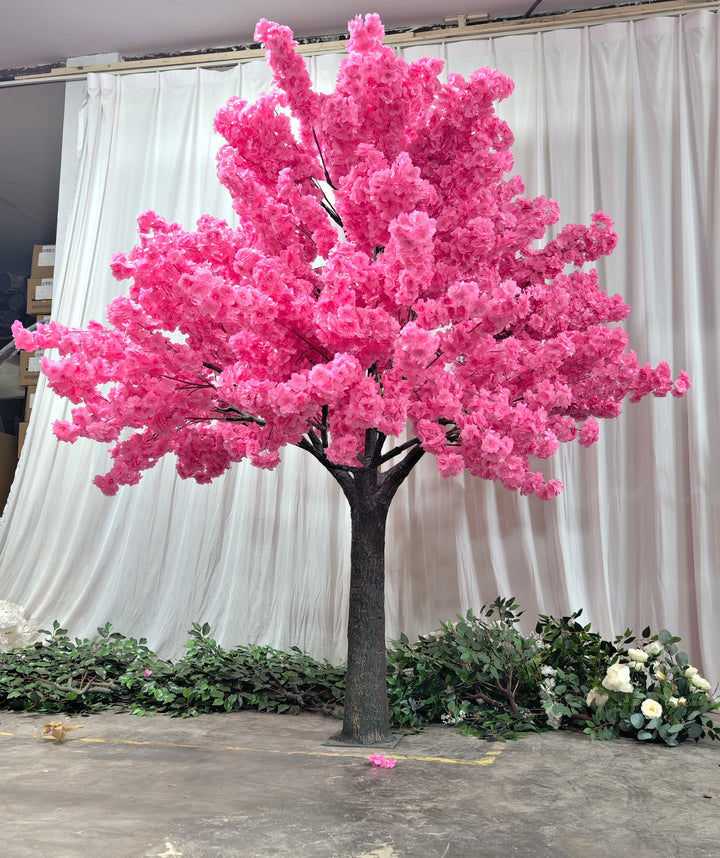 A stunning artificial dark pink cherry blossom tree with dense, vibrant flowers set against a white curtain backdrop, perfect for indoor decorations or events. 