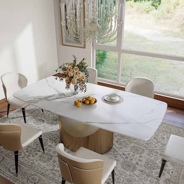 Alt text: "Elegant Dining Table with White Marble Surface and Gold Base, Decorated with a Floral Centerpiece and Lemons, Surrounded by Upholstered Chairs in a Bright Dining Room with Large Windows and a Luxurious Chandelier"