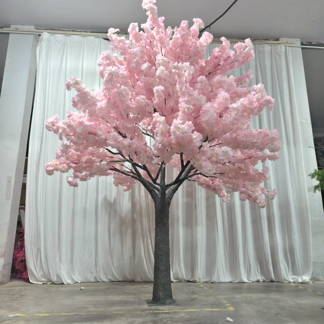 A stunning artificial pink cherry blossom tree displayed in a showroom with a white curtain backdrop. How durable are the blossoms against prolonged use and handling?