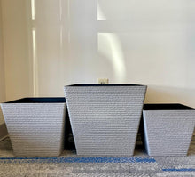 Load image into Gallery viewer, Three grey textured square planters, arranged side by side. The planters vary in size. The interior of each planter is black, providing a modern contrast to the white exterior.
