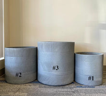 Charger l&#39;image dans la galerie, Cement planters. Three round, light gray planters in a minimalist design with horizontal ribbed texture. The planters are labeled with black numbers: #1 for the smallest, #2 for the medium size, and #3 for the largest. They are placed against a neutral wall with natural light filtering in.
