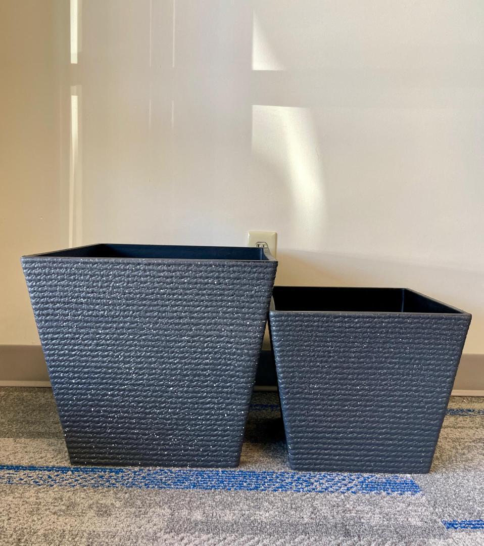Two black textured square planters, arranged side by side. The planters vary in size. The interior of each planter is black, providing a modern contrast to the white exterior.