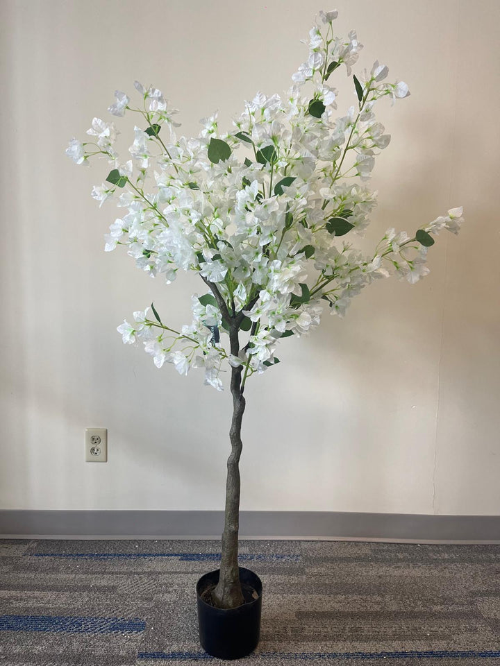 Artificial white flower tree with abundant blossoms in a modern white round planter, placed against a light-colored wall on a carpeted floor.