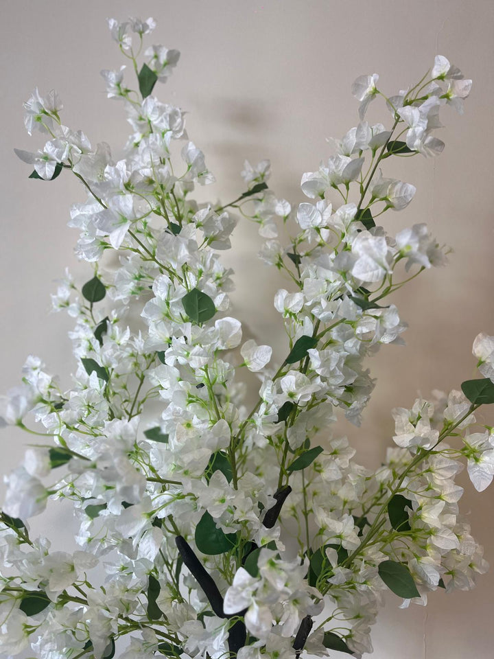 Close-up of an artificial white flower tree with delicate blossoms and green leaves, placed against a neutral-colored wall