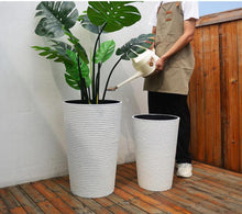 Load image into Gallery viewer, Two artificial tropical plants in tall, textured white planters placed indoors against a plain white wall. Common questions: What are the best large artificial plants for office or home interiors? How do I select tall planters for artificial plants? Are these planters suitable for both indoor and outdoor use?
