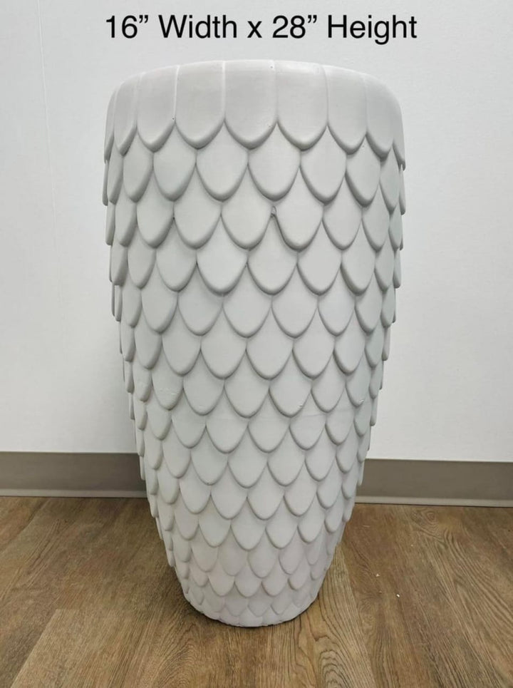 A tall white planter with a textured scale pattern, placed on a wooden floor against a neutral wall. What are the best plants to pair with textured planters for a modern home look?