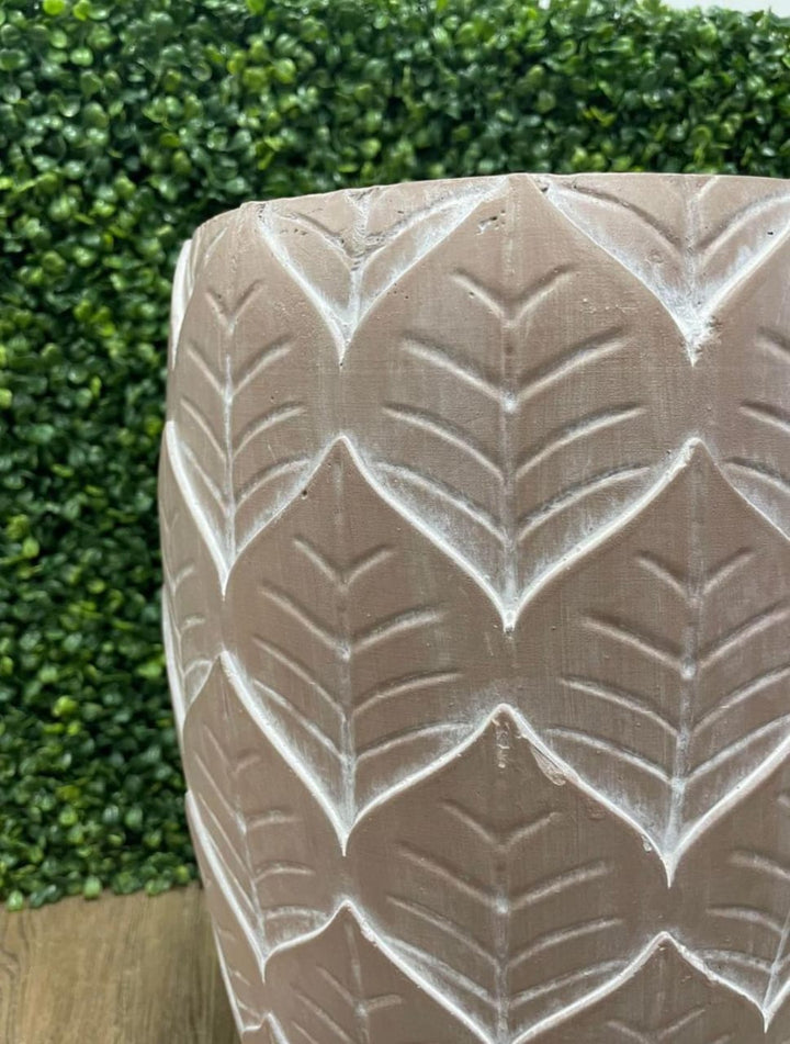 Close-up of a terracotta pot with a leaf pattern embossed, placed against a green leafy background. What are the best materials for indoor plant pots?