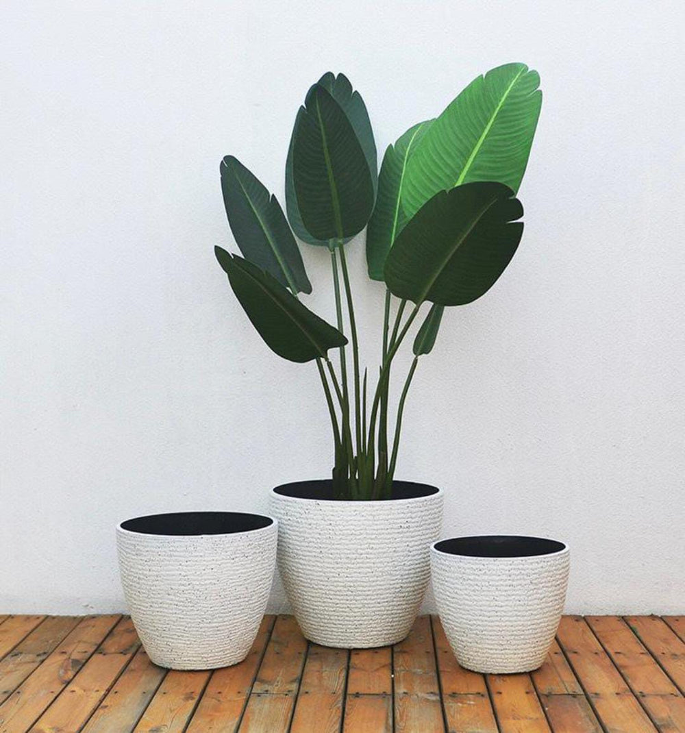 Artificial large leaf plant in a set of textured white outdoor planters on a wooden deck. Frequently asked questions: What size planter is best for tall artificial plants? How to select planters for different plant sizes? Are these planters durable for outdoor use?