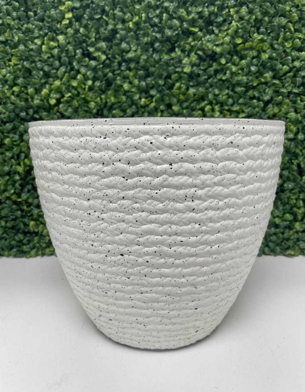 Textured white planter with a speckled finish displayed in front of a green leafy backdrop. Frequently asked questions: What materials are these planters made from? Are these planters suitable for both indoor and outdoor use? How to clean and maintain decorative planters?