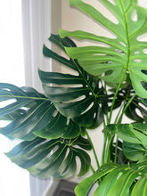 Charger l&#39;image dans la galerie, Close-up of artificial monstera leaves showcasing their large, glossy, dark green surface with realistic-looking veins and distinctive splits. The leaves are arranged against a neutral background, emphasizing their lush, tropical appearance
