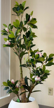 Load image into Gallery viewer, Artificial indoor tree with green leaves and pink flowers in a white round pot, placed in a modern interior setting with neutral tones.
