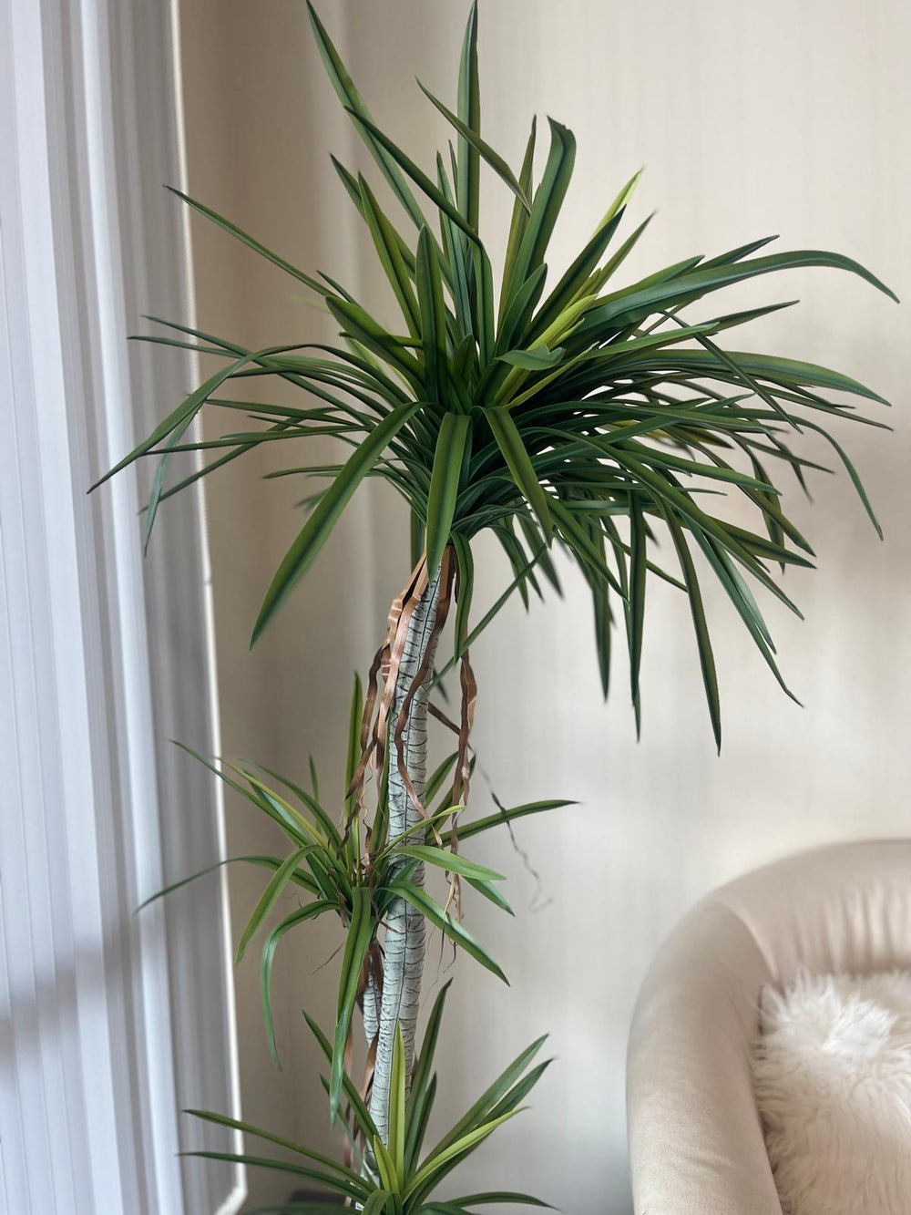 Close-up view of a tall artificial dracaena plant with realistic green leaves and brown decorative ribbon accents on the trunk, providing a detailed look at its lifelike design for home or office decor.
