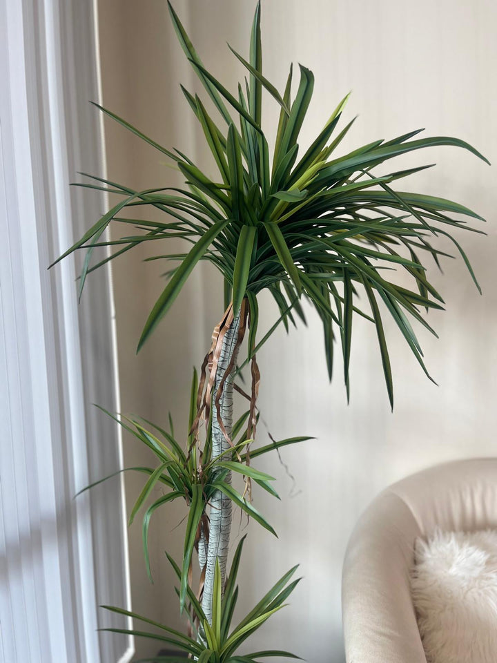 Close-up view of a tall artificial dracaena plant with realistic green leaves and brown decorative ribbon accents on the trunk, providing a detailed look at its lifelike design for home or office decor.