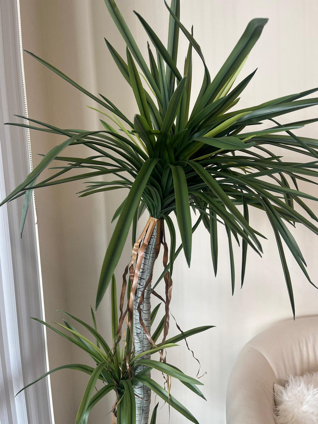 Close-up view of a tall artificial dracaena plant with realistic green leaves and brown decorative ribbon accents on the trunk, providing a detailed look at its lifelike design for home or office decor