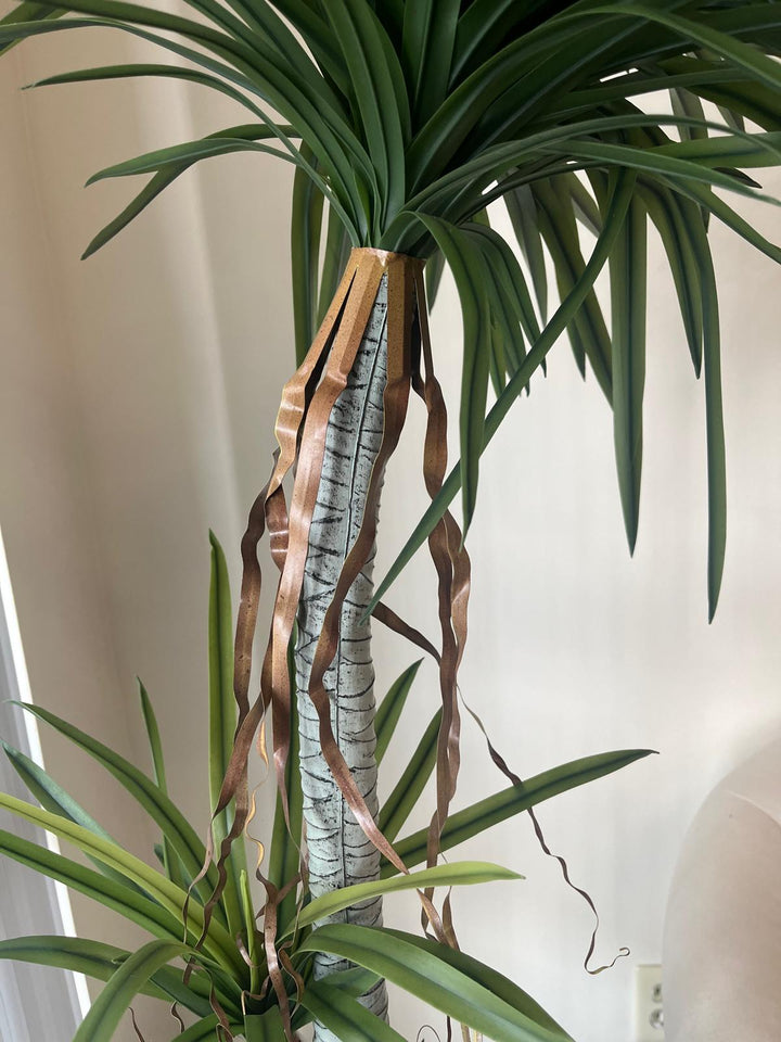 Close-up view of a tall artificial dracaena plant with realistic green leaves and brown decorative ribbon accents on the trunk, providing a detailed look at its lifelike design for home or office decor.