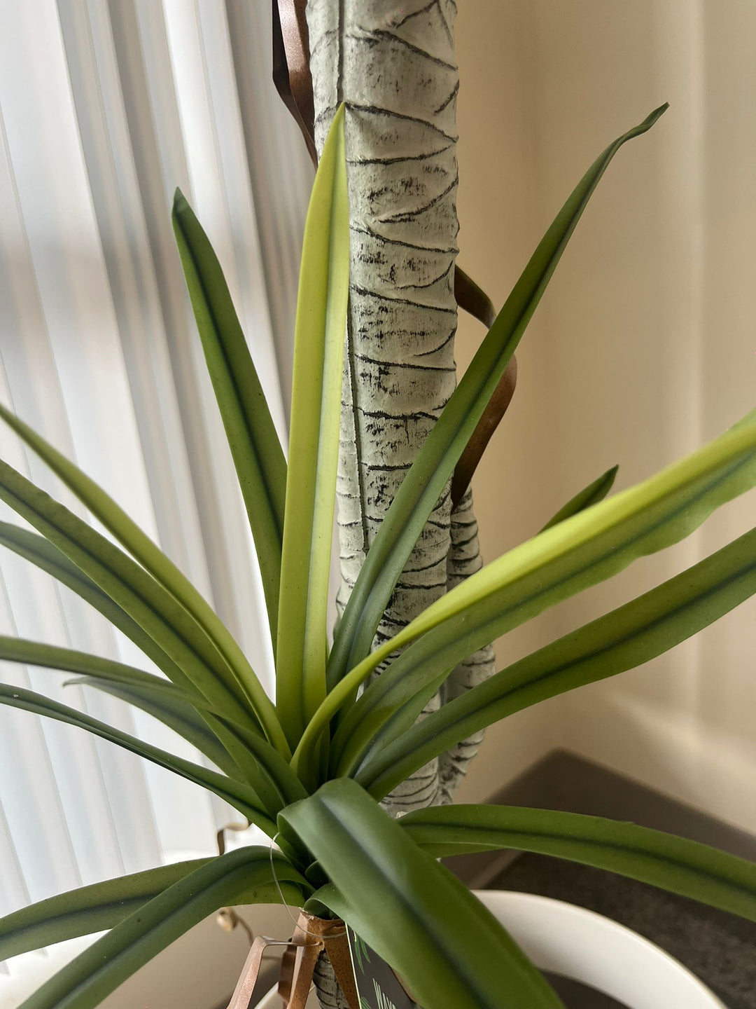 Close-up shot of the base of an artificial dracaena plant, featuring realistic green leaves and a textured faux trunk, showcasing the intricate detail for indoor home or office decor.