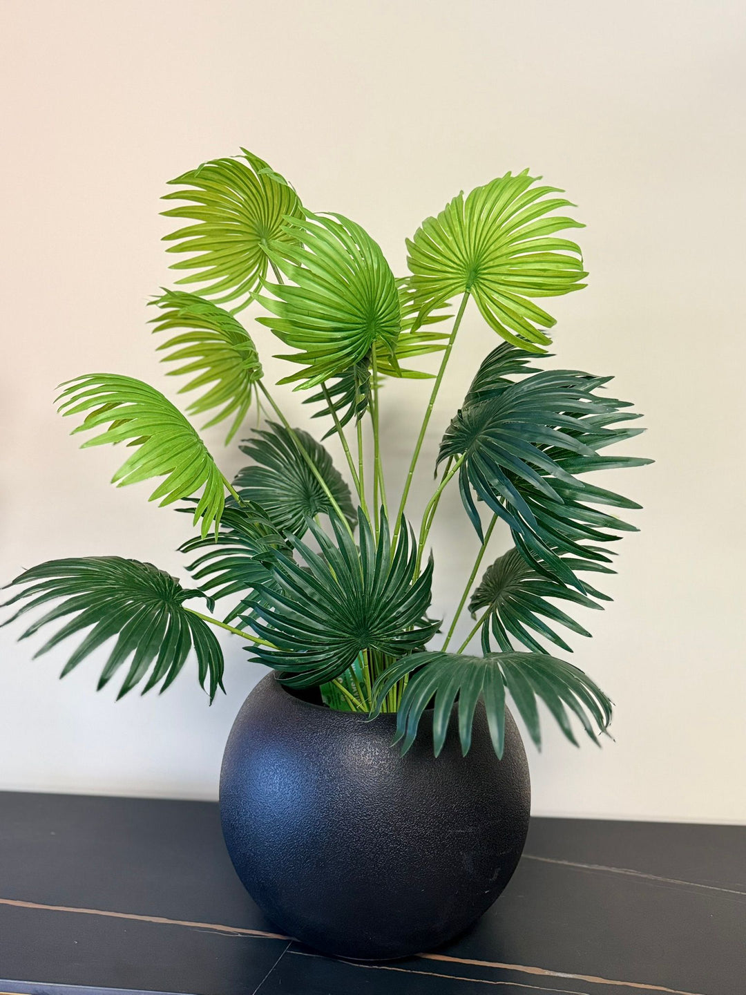 Tabletop faux fan palm plant in a decorative lack pot on wooden shelf in contemporary interior