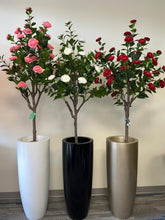 Charger l&#39;image dans la galerie, Three artificial flowering trees are displayed in sleek, tall planters in white, black, and gold. The trees feature vibrant pink, white, and red blossoms, creating a striking contrast against the green leaves. The arrangement adds a pop of color to the minimalist indoor space with a neutral beige wall as the background.
