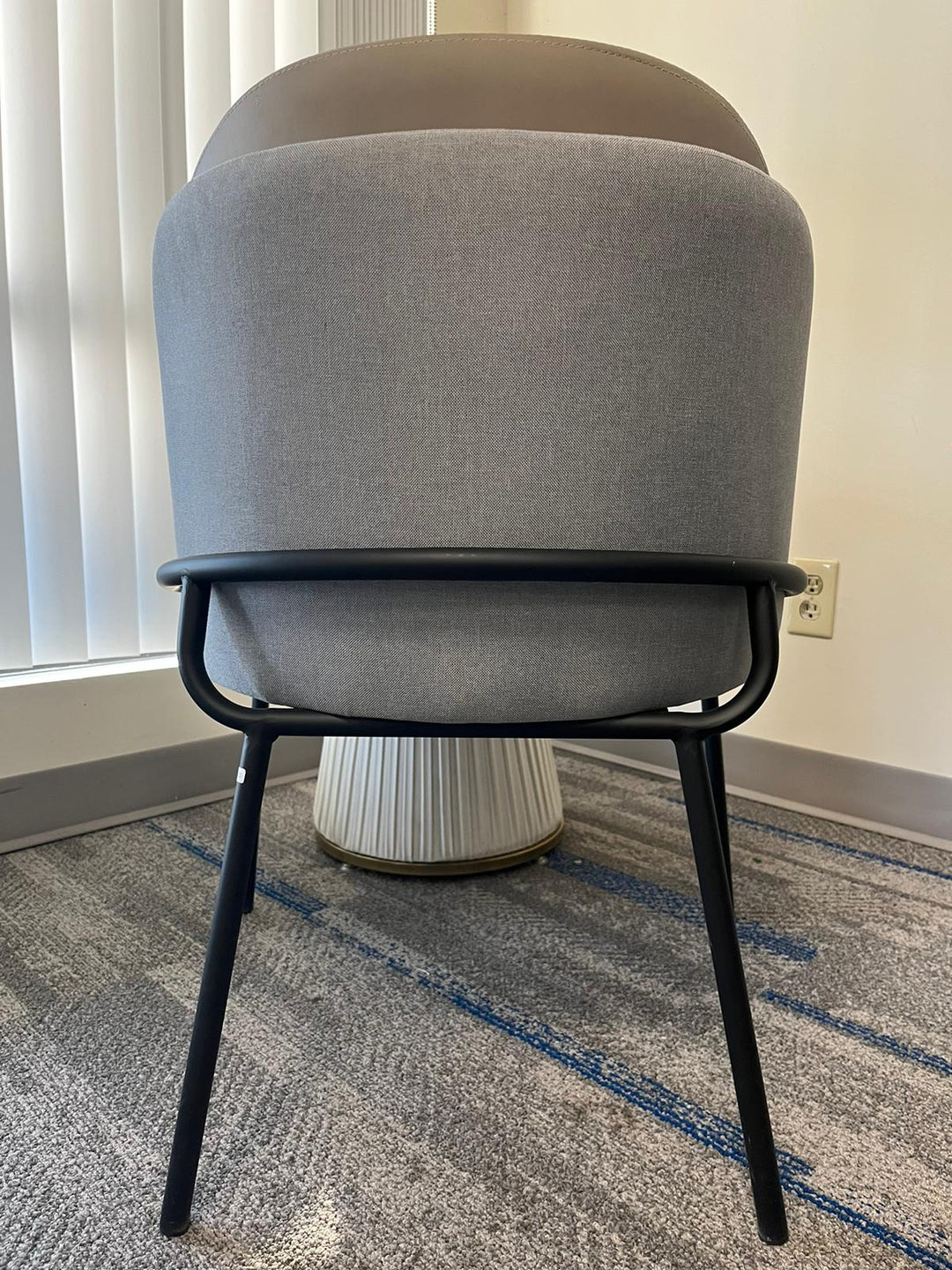 Back view of a modern gray upholstered chair with a black metal frame, often chosen for its contemporary style and comfort. Frequently asked questions about this chair include ‘What are the best chairs for lumbar support in small spaces?’ and ‘How do modern chairs enhance home office setups?