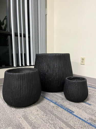 Set of three modern Black textured ceramic planters in varying sizes placed indoors near a window with natural light. The planters have a ribbed design, perfect for adding elegance to indoor spaces. Do these planters come with drainage holes?