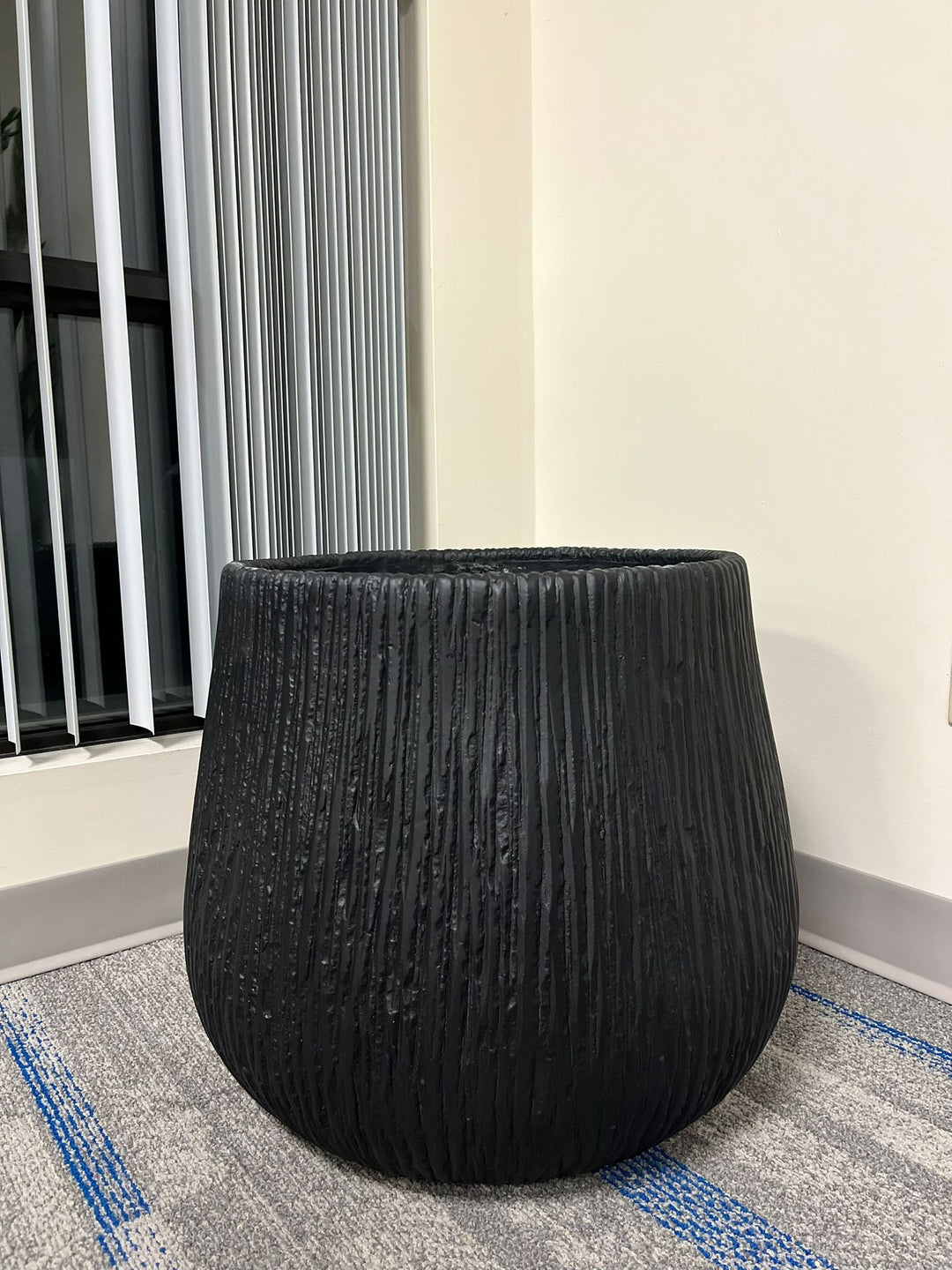 Large black textured planter with a modern ribbed design, placed indoors near a window with natural light. What are the dimensions of this planter?