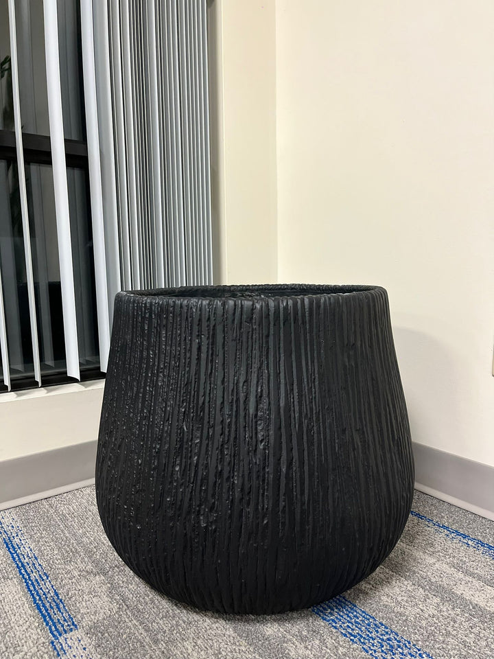 Large black textured planter with a modern ribbed design, placed indoors near a window with natural light. What are the dimensions of this planter?