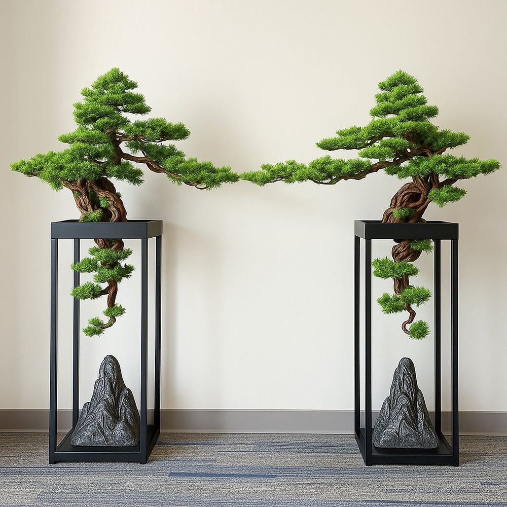 Two artificial bonsai trees with lifelike foliage on black stands with sculptural rock bases.