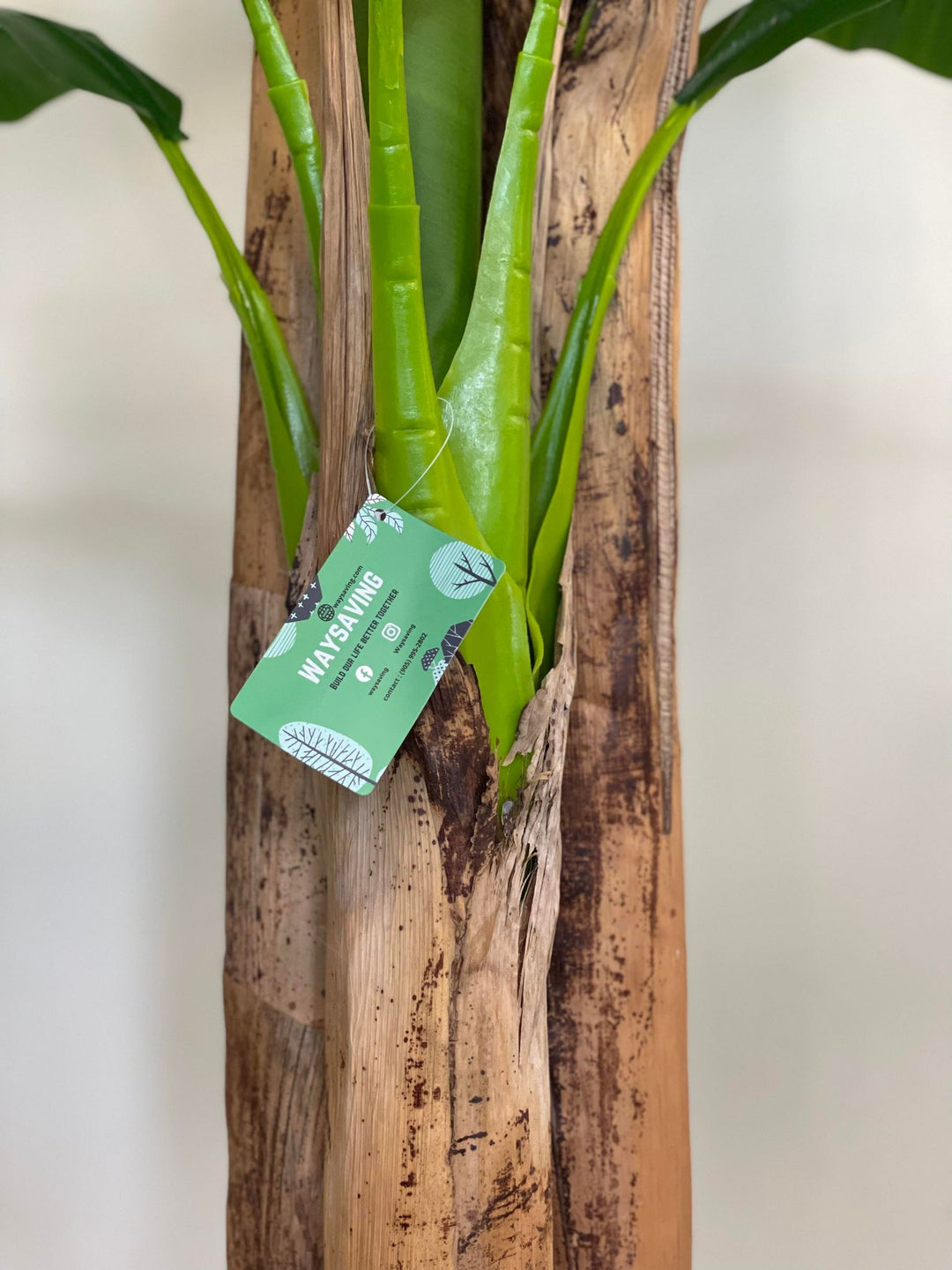 Close-up of an artificial banana tree trunk with detailed texture, highlighting the lifelike appearance and attached product tag, suitable for indoor decoration.