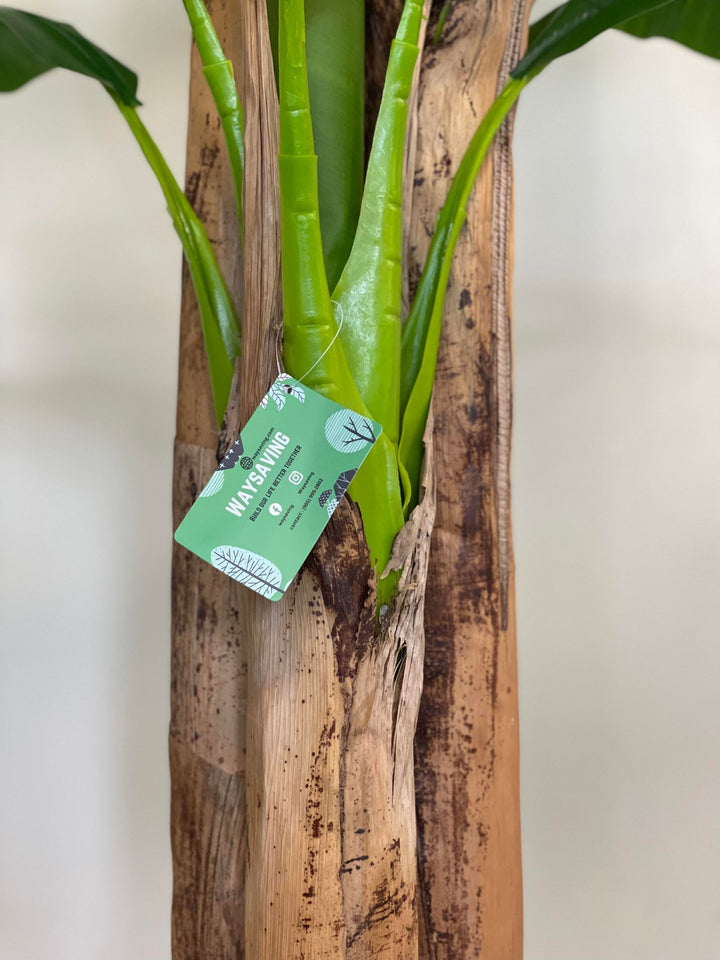 Close-up of an artificial banana tree trunk with detailed texture, highlighting the lifelike appearance and attached product tag, suitable for indoor decoration.