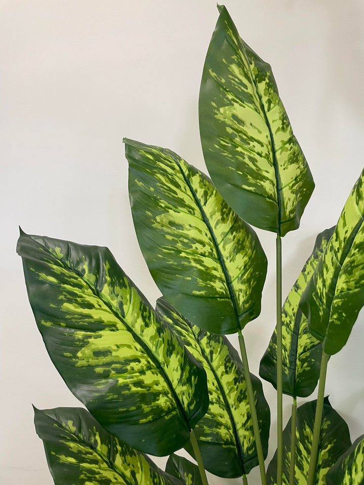 Close-up of the vibrant, variegated leaves of a tall artificial Dieffenbachia plant, showcasing the intricate patterns of green and yellow.