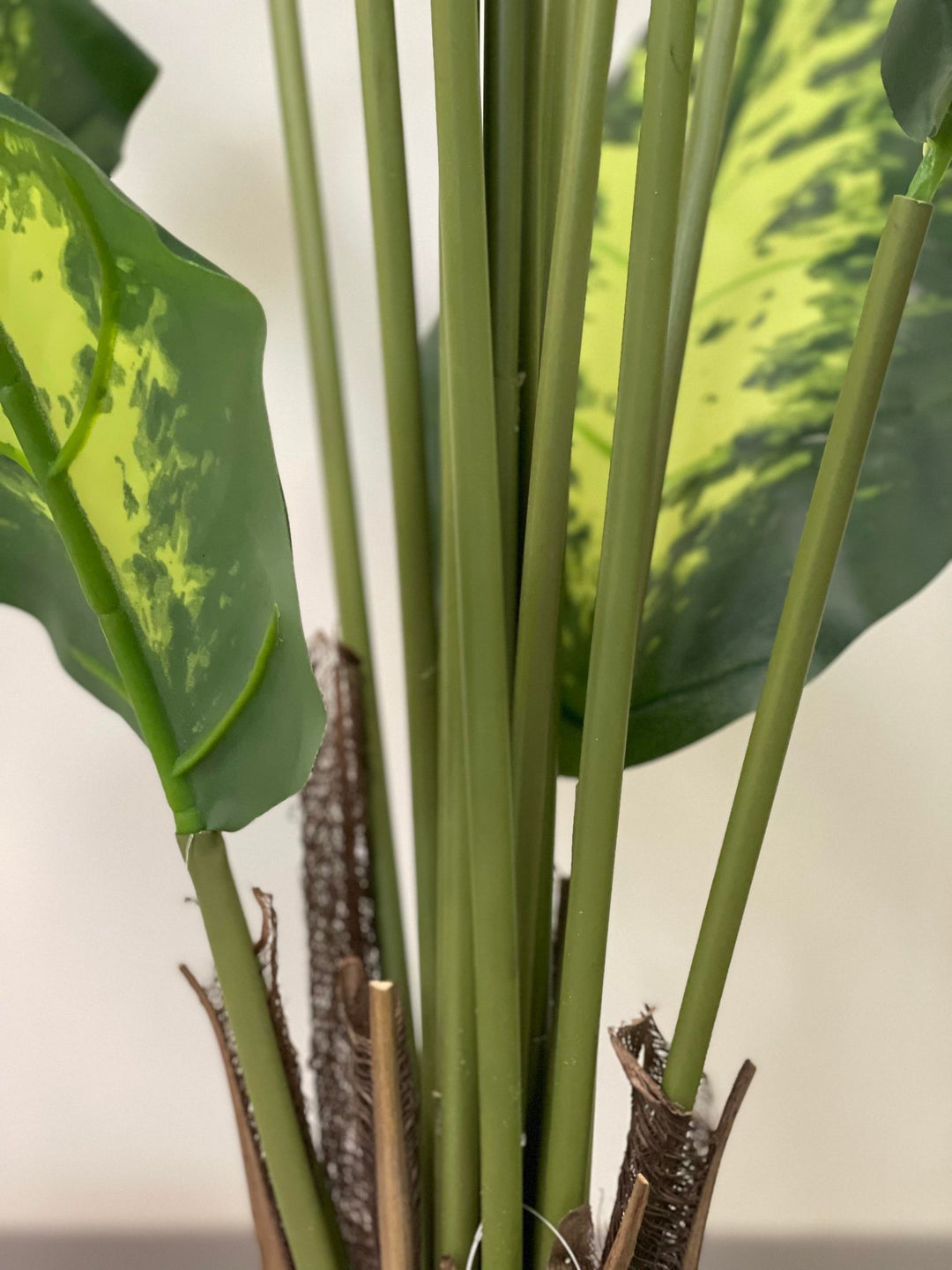 Close-up of the stems of an artificial Dieffenbachia plant, highlighting the realistic texture and detailing at the base.