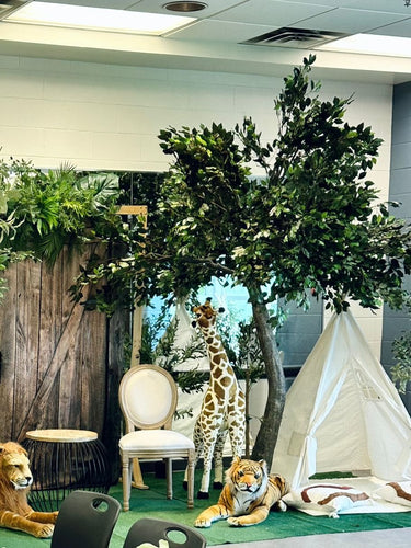 A 10ft artificial Ficus tree with dense, vibrant green leaves, ideal for creating a jungle-themed atmosphere, surrounded by floral decorations and boxes in an indoor setting.