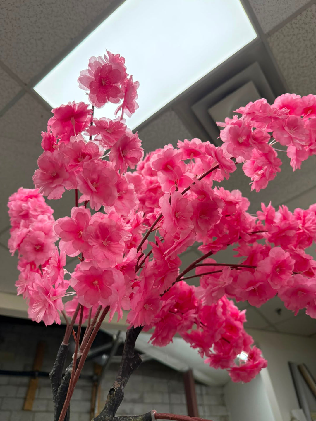 Bright pink artificial cherry blossom tree branches with dense clusters of layered flowers on dark brown stems.