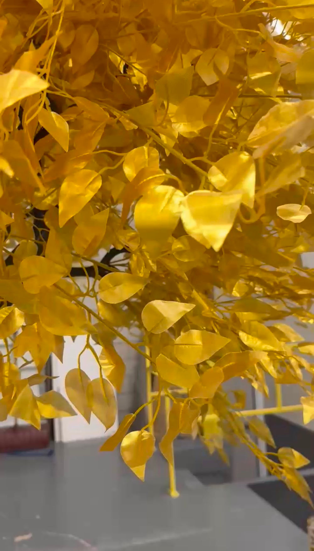 A close-up of a golden yellow artificial ficus leafy vine or decorative branch with heart-shaped leaves, shown against a blurred indoor background.