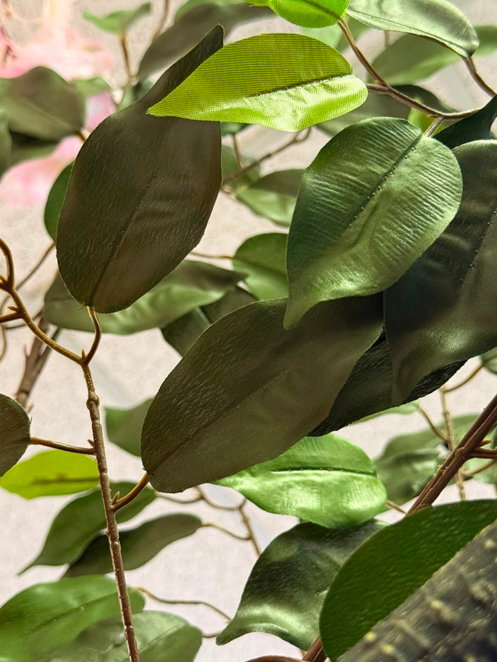 Close-up of artificial green ficus leaves with a metallic, satin-like sheen attached to thin brown branches.