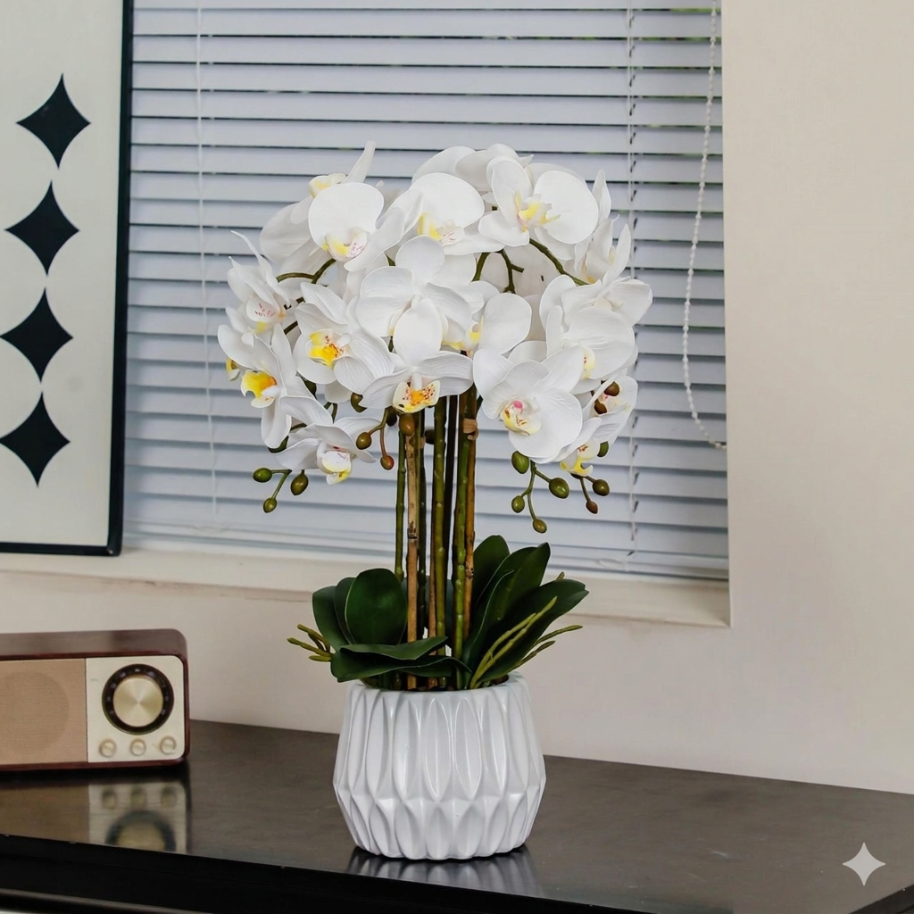 White orchid in a decorative vase on a table with a window and wall art in the background.