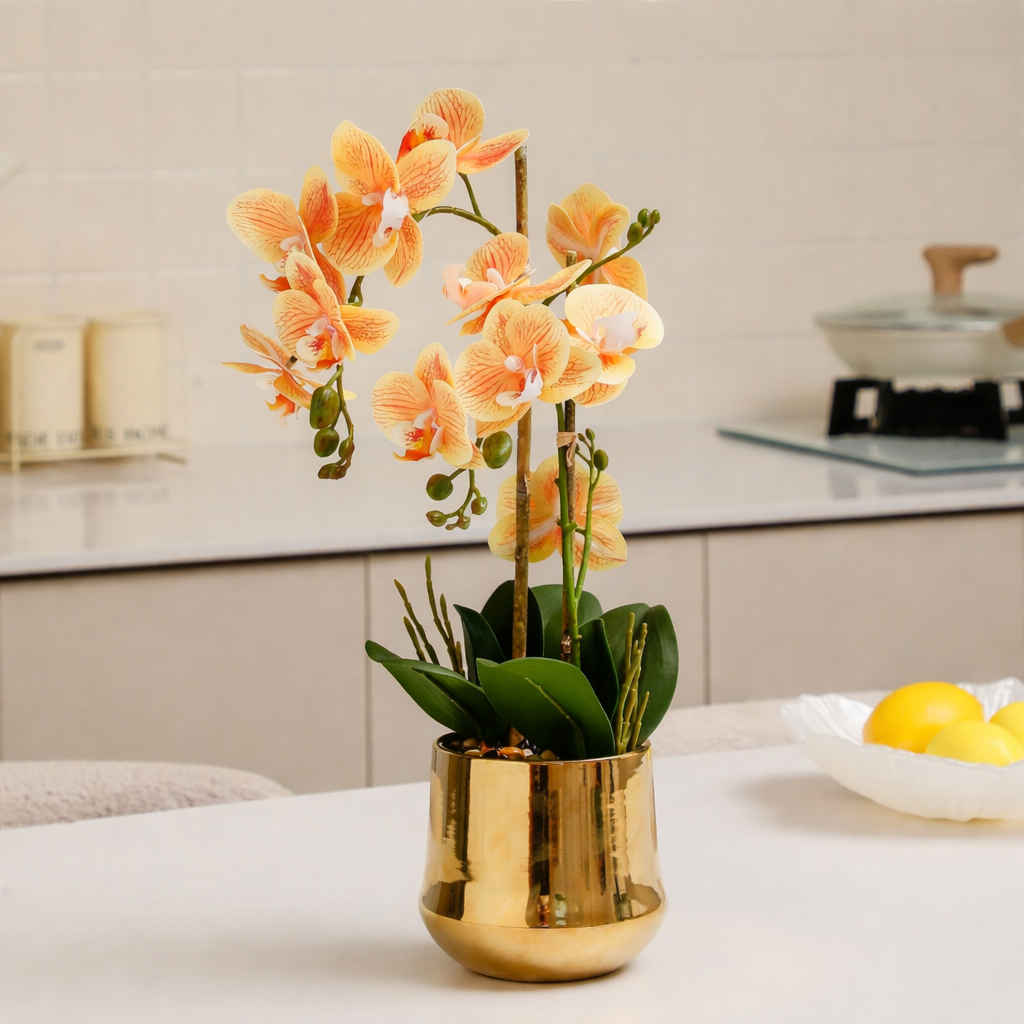 Vibrant orange colored orchid arrangement placed in a gold pot placed on a kitchen counter.