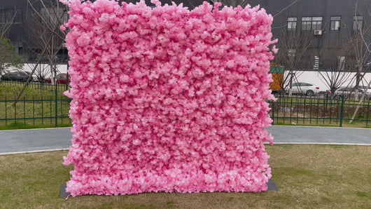 Large pink artificial flower wall backdrop set up outdoors, commonly used for events like weddings, parties, and photoshoots. Is this flower wall backdrop weather-resistant? How easy is it to assemble and transport? Can it be customized in other colors?