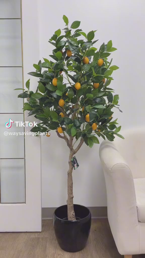 Artificial lemon tree with lush green leaves and bright yellow lemons in a tall black planter, placed near a glass-paneled door in a modern indoor setting