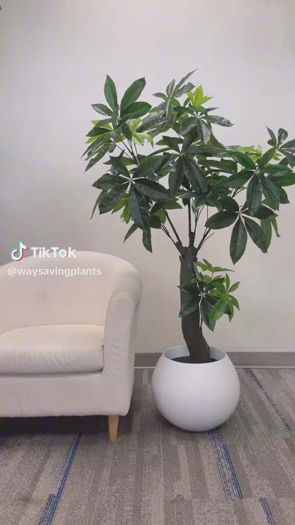 Artificial money tree with lush green leaves in a modern white planter next to a cream-colored armchair in a contemporary indoor setting