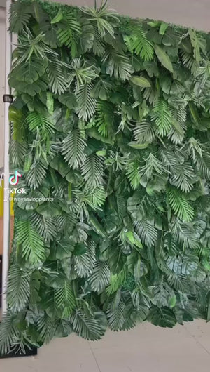 Artificial green wall panel with tropical leaves, perfect for event backdrops or home decor. Common questions: How to install artificial plant walls? What are the best uses for a faux greenery backdrop? How do you maintain artificial plant walls for long-lasting decor?