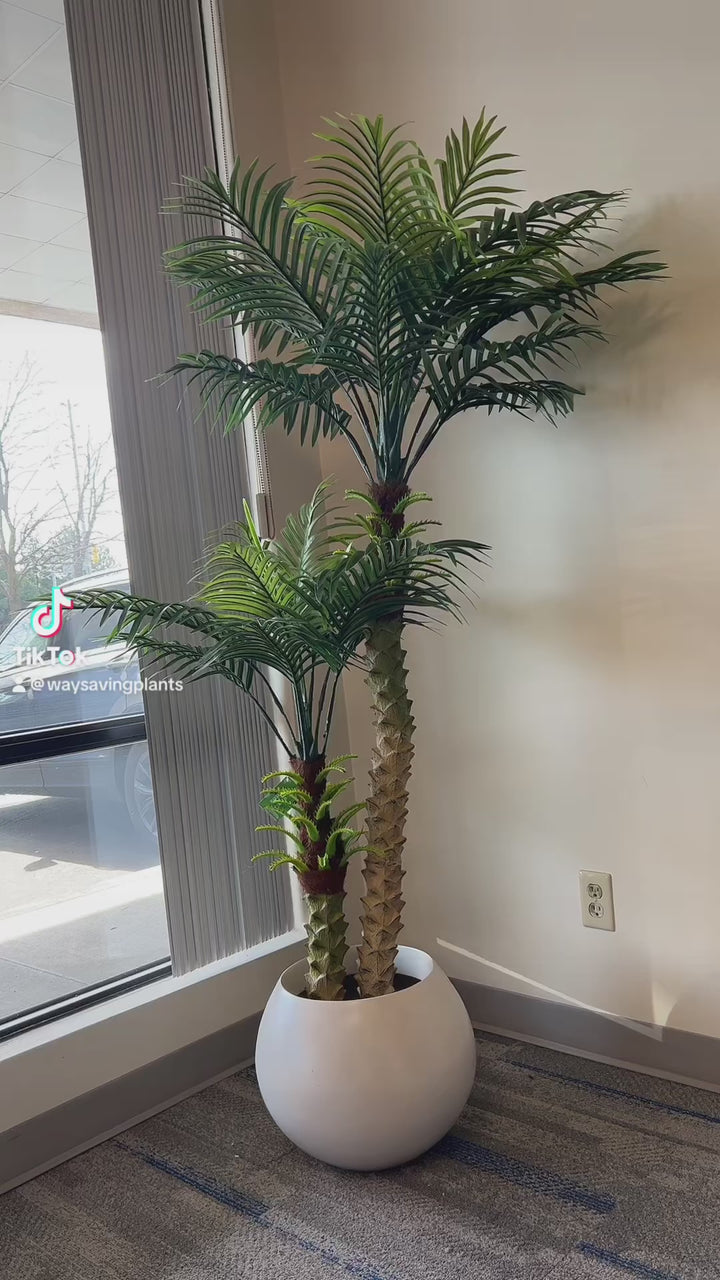 Artificial palm tree with multiple fronds displayed by a large window, adding tropical ambiance to the space.