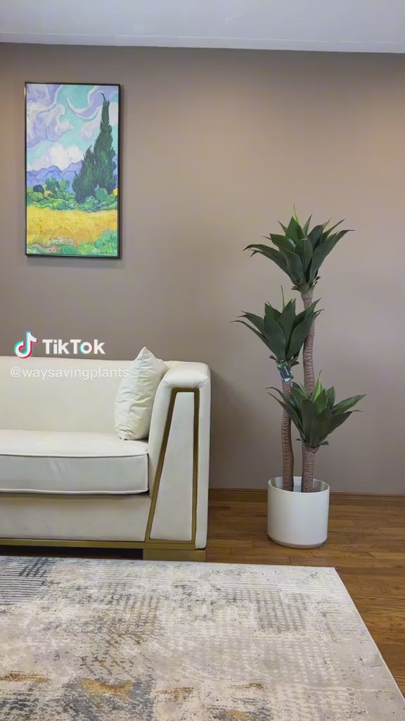 Modern living room setup featuring a cream-colored sofa with a faux yucca agave plant in a white pot next to it. The artificial plant adds greenery to the minimalist decor, enhancing the stylish interior design.