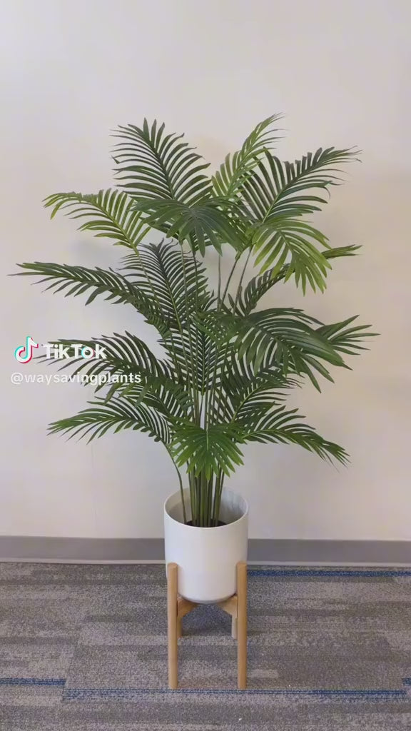 Modern office decor with a vibrant green palm plant in a sleek white planter, elevated on a wooden stand against a neutral wall.